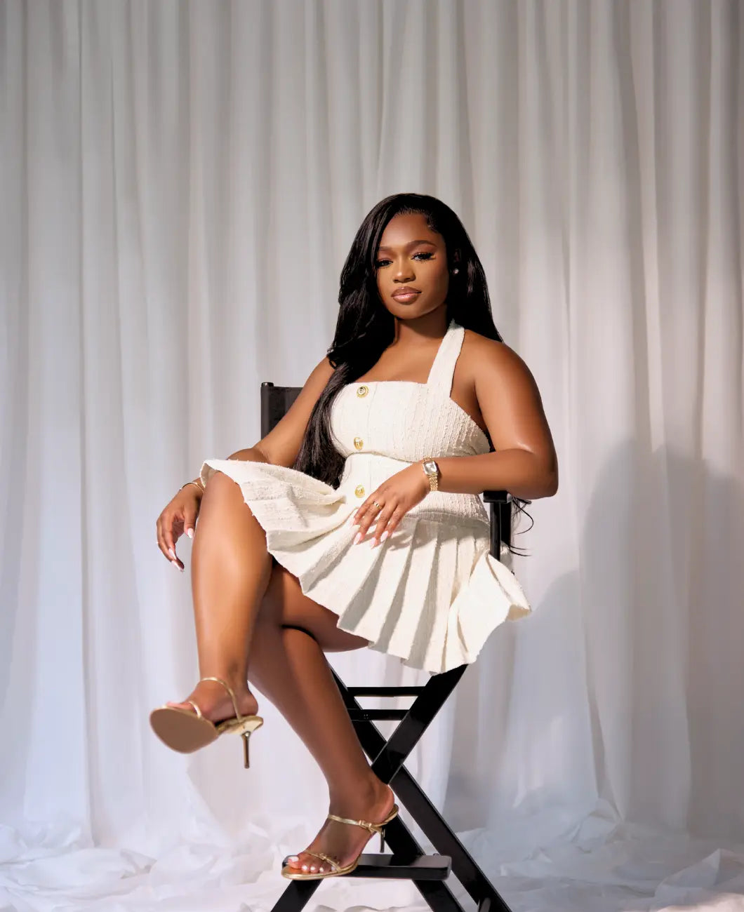 Black Woman in a white dress sitting on a chair against a white curtain
